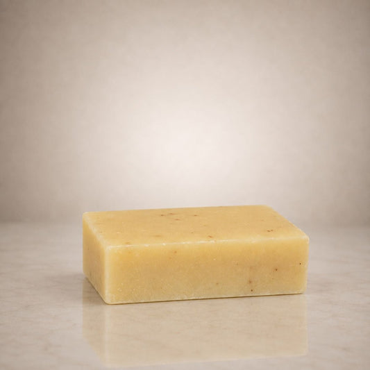 A rectangular bar of pale yellow soap with small brown specks, standing on a light marble surface against a neutral beige background.