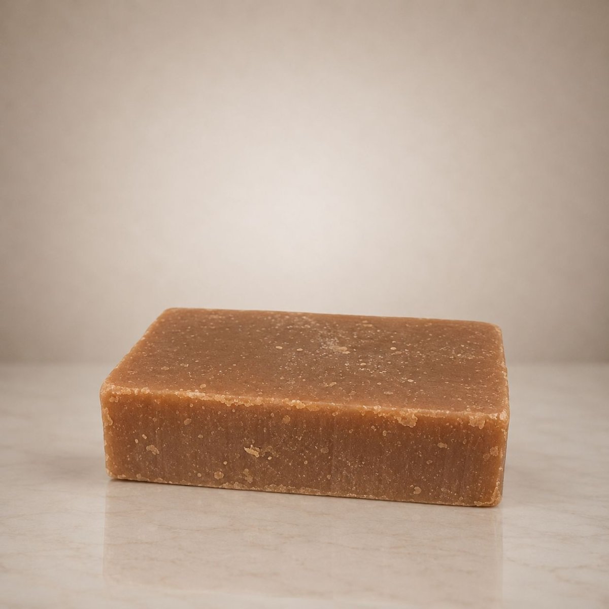 A rectangular bar of natural brown soap with a rustic, textured surface, displayed on a light marble surface against a neutral beige background.