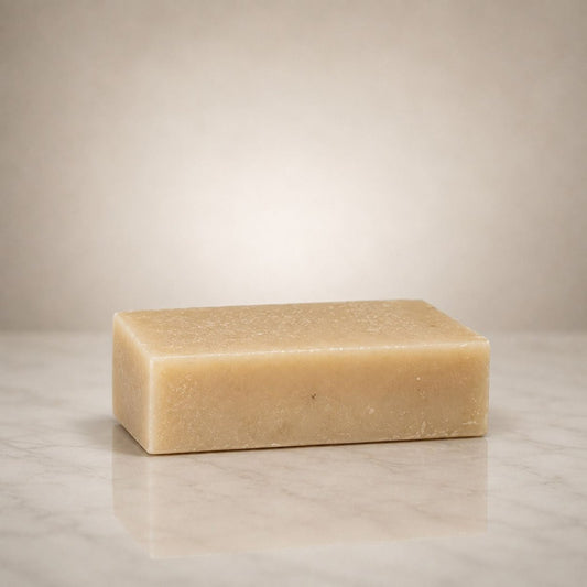 A rectangular bar of pale beige soap standing upright on a light marble surface against a softly lit neutral background.
